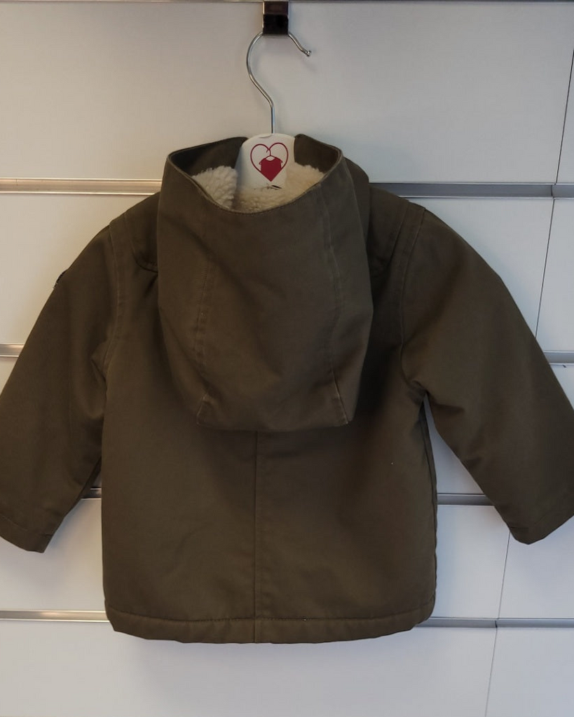 Brown children's jacket on a hanger against a white wall.